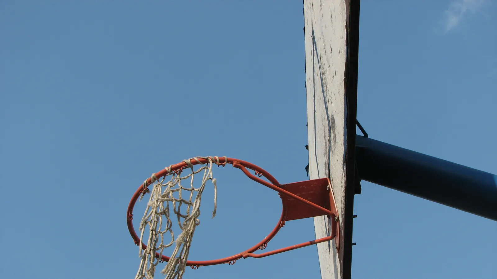 Panneau et cercle de basketball en extérieur, filet usé, sur fond de ciel bleu
