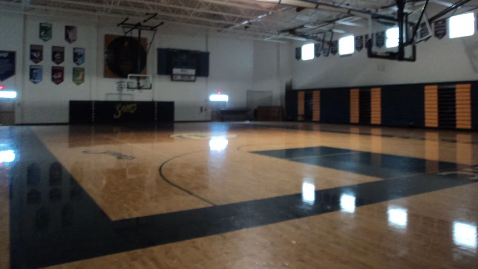 Gymnase vide avec parquet, panneaux de basketball et tableau d'affichage au fond de la salle